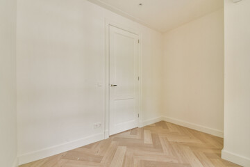 A bright and airy corner of a minimalist interior showcasing a door against a light-colored wall, complemented by a herringbone patterned floor.