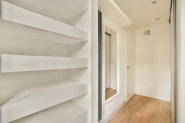 A clean and minimalist hallway featuring sleek white shelves and a mirror with natural wood...