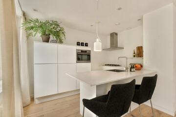 A sleek, modern kitchen featuring a white island, stylish chairs, and natural light, creating a bright and inviting atmosphere for culinary activities.