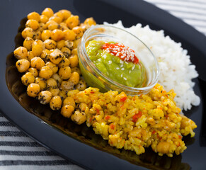 Black plate with spicy garbanzos, two types of rice and red and green sauces..