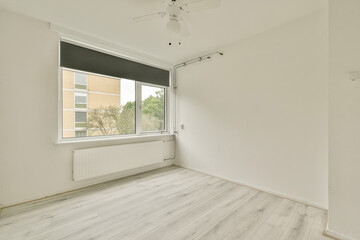 Fototapeta premium A minimalist interior featuring white walls and flooring, with a large window allowing natural light. The space is simple yet inviting, suitable for various decor styles.