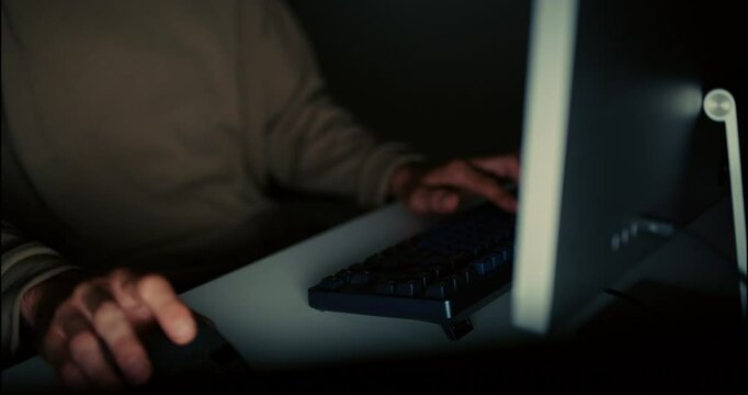 Close-up shot of a hacker or programmer&rsquo;s hand using mouse and keyboard in low light, working on cybersecurity tasks or coding late at night.