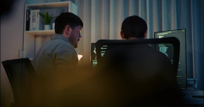 Two developers collaborating on programming at night, focused on computer screens filled with code in a modern software development workspace.