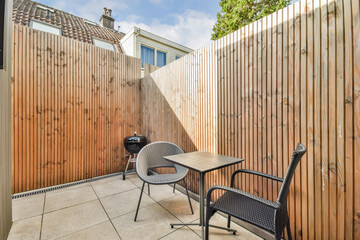 A serene outdoor patio features wooden fencing, a small table with chairs, and a barbecue grill,...
