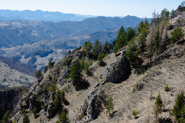 Scenic view of a mountainous landscape with rugged terrain and scattered trees under a clear blue sky.