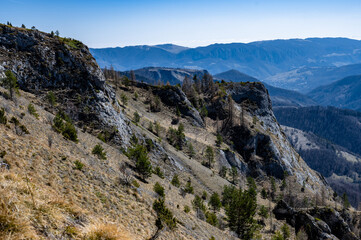 A stunning mountain landscape with rocky cliffs and sparse trees under a clear blue sky, showcasing natural beauty and tranquility