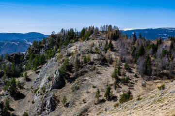 A scenic view of a rugged mountain landscape with sparse trees under a clear blue sky in a remote area.