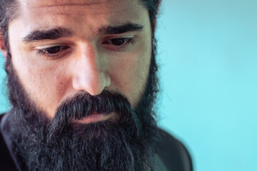 A close-up portrait of a thoughtful man with a beard, appearing reflective and serene, set against a blue background.