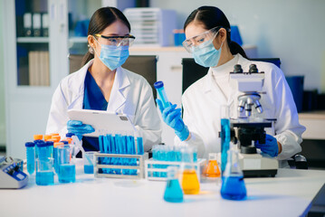 Fototapeta premium Two Asian female biotechnologists in lab coats conduct research, handle glassware, and test chemicals in a modern science lab