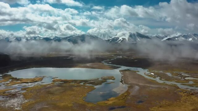 Drone footage captures the stunning lakes of Arabel Plateau, Kyrgyzstan, surrounded by lush green landscapes and snow-covered mountains, with the drone flying amidst clouds.