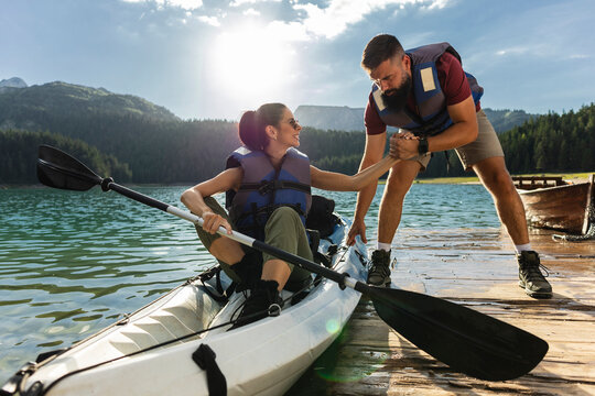 Man helping woman getting out of kayak on mountain lake