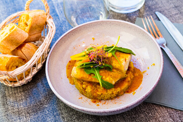 Closeup of codfish baked with curry and served with quinoa and greens at plate..