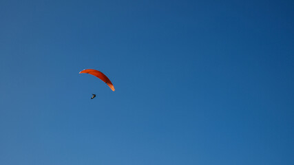 Paraglider with orange wing soaring against clear blue sky backdrop