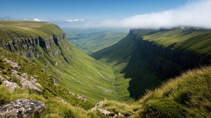 Naklejka premium Mountain valley view, vibrant green landscape, rugged peaks, mist in distance