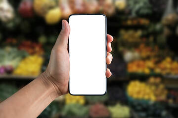 Hand Holding a Blank Smartphone with Colorful Fruits and Vegetables in the Background at a Fresh Produce Market Stand. Agnostic