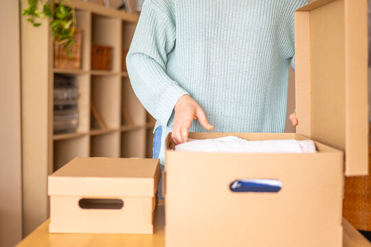 Woman unpacking clothes from a cardboard box after moving into a new house, carefully organizing belongings and embracing a fresh start in her new living space
