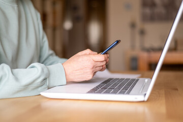 Close up of  hands holding smartphone while working or studying with laptop at home, concept of smart working, technology, social media, communication, internet, learning