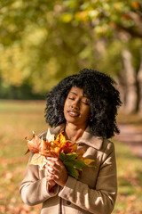 Naklejka premium Woman holding an autumn leaves bouquet and sunbathes on a sunny day in October.