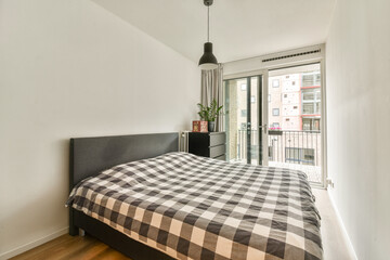 A stylish and contemporary bedroom featuring a checkered bedspread and a balcony overlooking an urban environment, showcasing modern design elements.