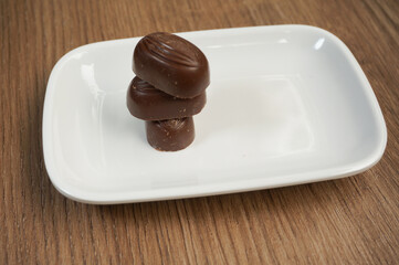 stack of chocolates, on a white square plate, wooden background,