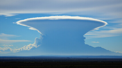 A single, anvil shaped cloud dominates the horizon, its flat top reaching high into the atmosphere