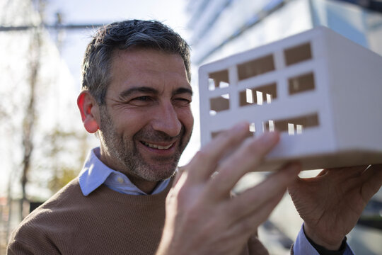 Architect smiling while holding a building model outdoors