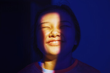 Cheerful girl with closed eyes in blue and yellow light