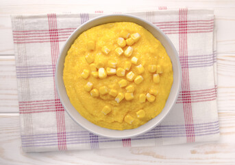 Delicious corn porridge in a bowl on a white wooden table.