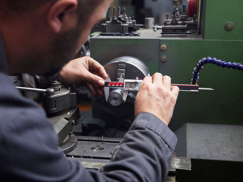 Metal construction technician measuring with calipers at a lathe in a workshop