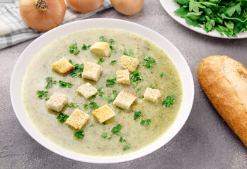 Homemade cream soup with chicken and herbs in a white plate on a gray background.