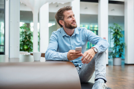 Young man in a modern office holding a mobile phone and smiling