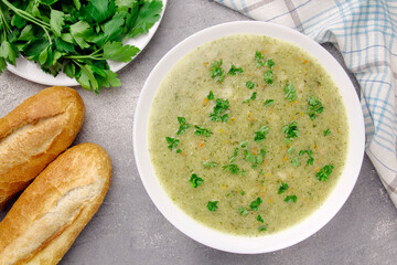 Homemade cream soup with chicken and herbs in a white plate on a gray background.