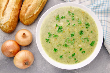 Homemade cream soup with chicken and herbs in a white plate on a gray background.
