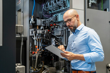 Engineer inspecting machinery in a production hall using a tablet