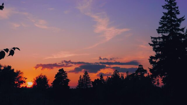 Evening sky at sunset background in forest. Dark clouds hanging above horizon. Majestic cloudscape in blue, orange, violet shades. Grey cloudlets bringing rain. Countryside skyline in twilight time