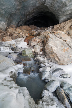 Snow, meltwater stream, and rocks in ice cave below glacier