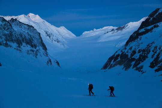 Backcountry skiers ascend mountain pass at dawn above Aletsch Glacier