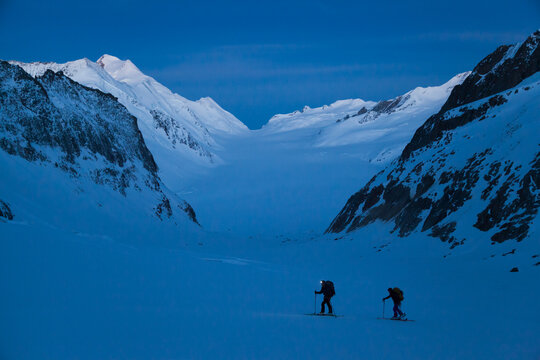 Backcountry skiers ascend mountain pass at dawn above Aletsch Glacier