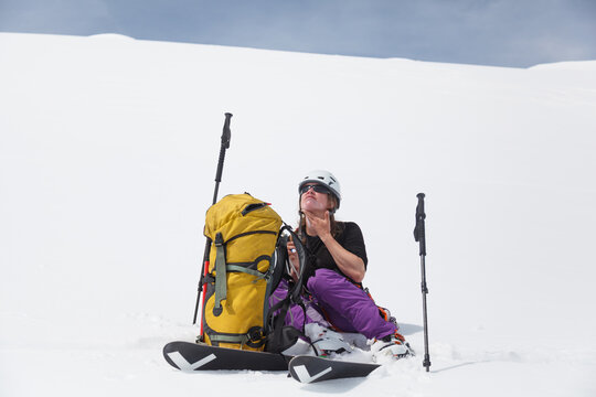 Woman backcountry skier sits in bright snow to apply sun screen