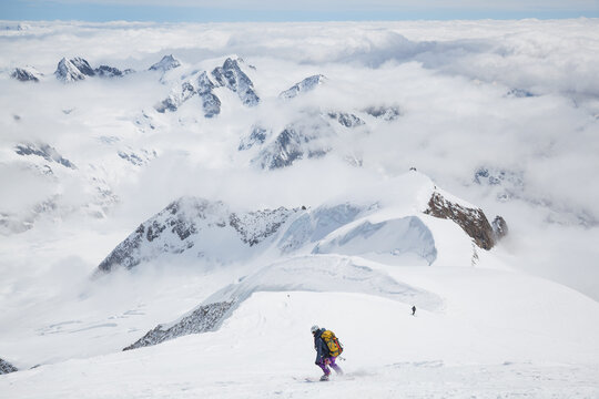 Backcountry skiers descend from mountain summit above low clouds
