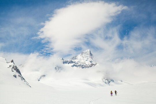 Backcountry skiers cross Fiescher Glacier below jagged mountain peak