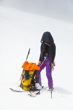 Backcountry skier stands in snow with jacket on head against sun