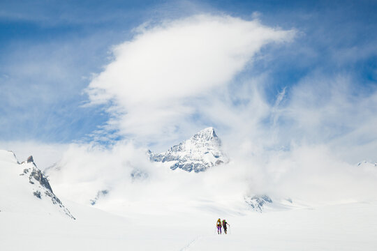 Backcountry skiers cross Fiescher Glacier below jagged mountain peak