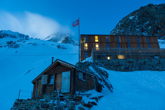 Finsteraarhorn Hut and Swiss flag at dusk below snow-covered mountains