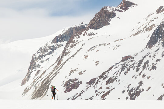 Backcountry skier crosses glacier towards mountain hut on steep slope