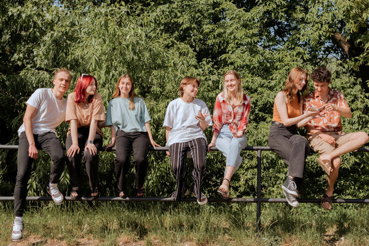 Teens sitting and talking on fence in sunny park