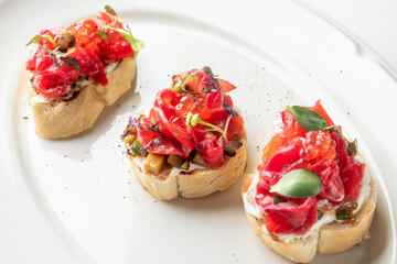 Three delectable bruschettas topped with fresh diced tomatoes, herbs, and olives, elegantly presented on a white plate. Perfect for appetizers or party platters.