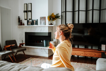 Woman in a yellow sweater sitting on a couch with a coffee cup in a cozy living room
