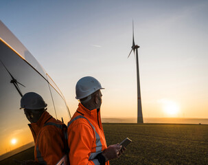 Engineer with tablet observing wind turbine at sunset