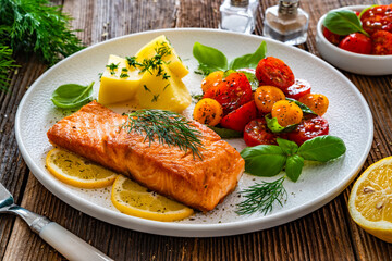 Seared salmon steak with cherry tomatoes and boiled potatoes on wooden table